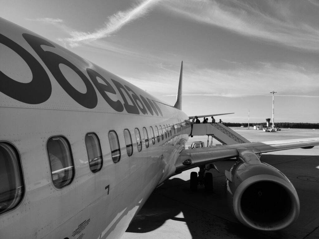 pexels-photo-13343879-13343879 Monochrome image of an airplane on the tarmac with passengers boarding via stairs.