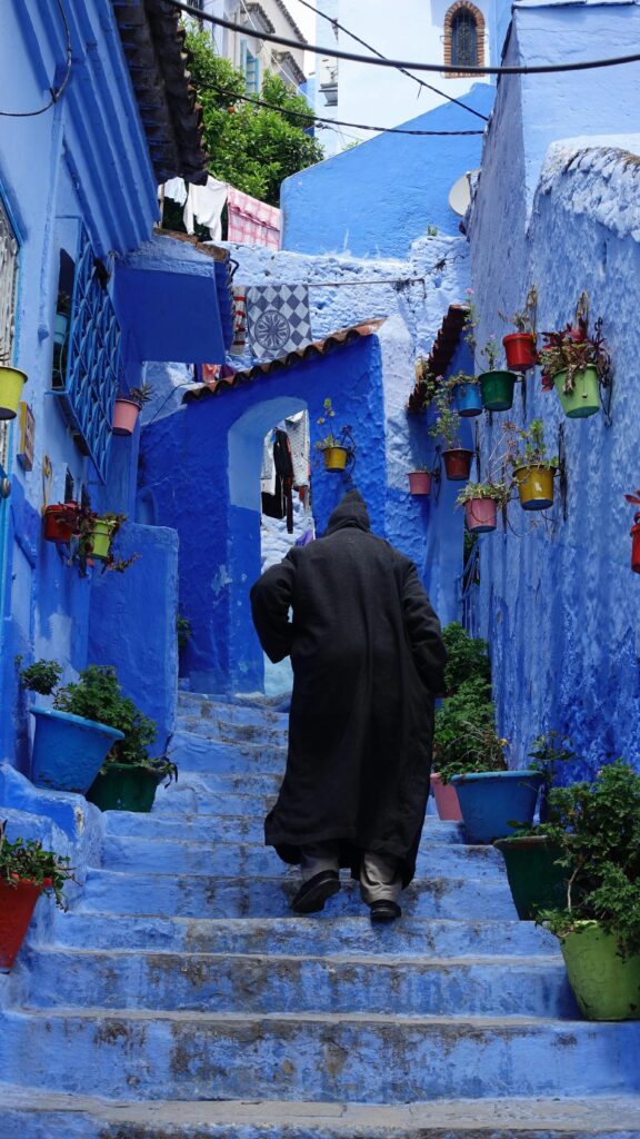 Man in traditional robe walks through Chefchaouen's vibrant blue alley, Morocco.