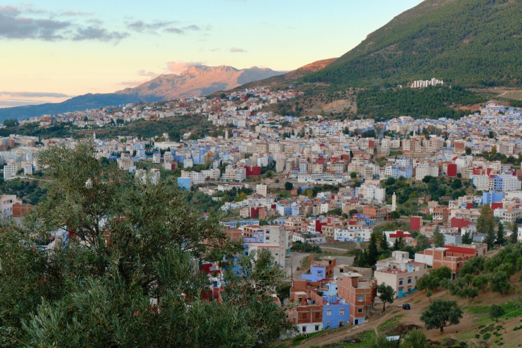Discover the vibrant architecture of a Moroccan city nestled in a breathtaking mountain valley under a serene sky.