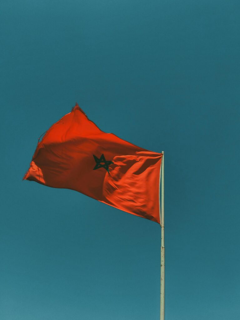 Red Moroccan flag waving against a blue sky, symbolizing national pride.