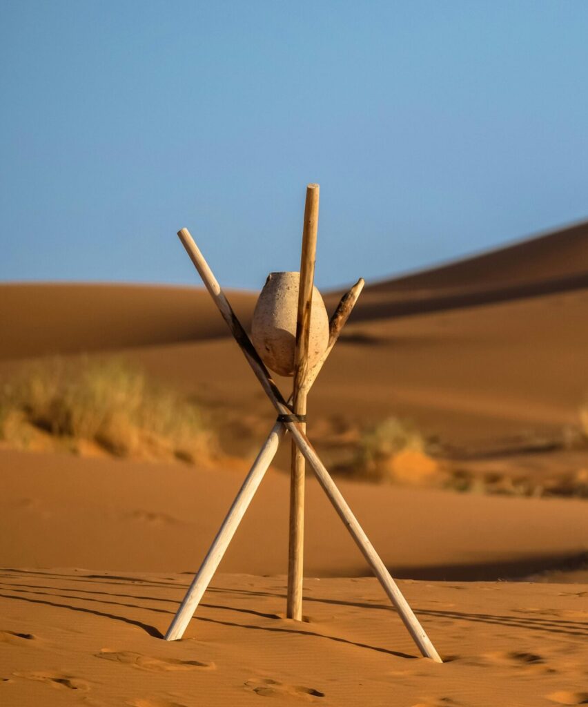 Peaceful desert landscape at Merzouga with sand dunes and wooden tripod under clear blue sky.