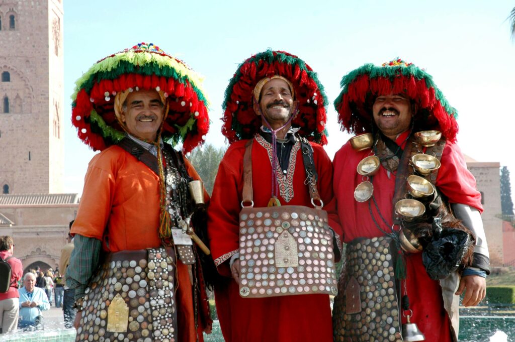 Three Moroccan men in traditional attire posing at a landmark in Marrakech.