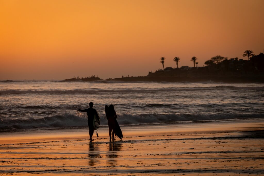 A beautiful sunset on the beach in Taghazout, Morocco, with surfers walking along the shore.