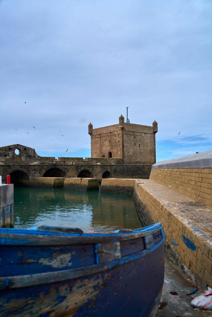 Scenic view of the historic bastion with a docked boat in Essaouira, Morocco, under a bright sky.