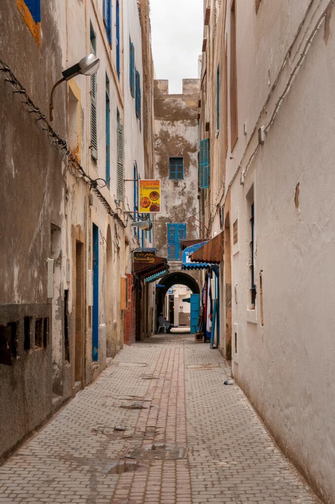 Empty narrow paved street between old shabby residential buildings with wooden windows located in Essaouira