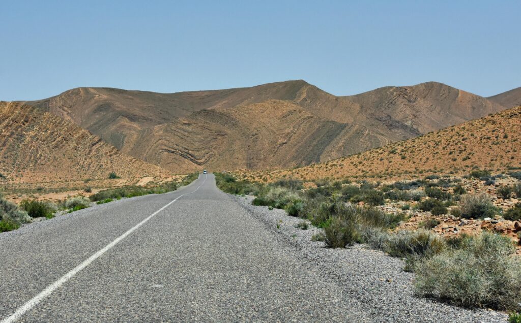 Long winding road through Moroccan mountains near Irherm under a clear blue sky.